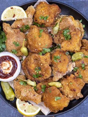 Fried oyster mushrooms garnished with pickled chili, lemon wedges and ketchup and mayo sauce on a plate.