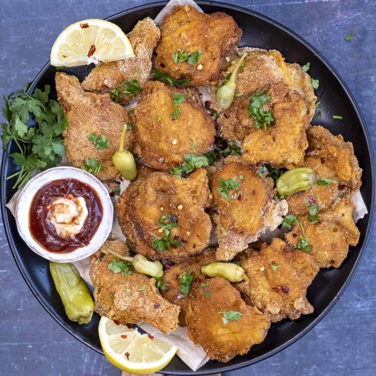 Fried oyster mushrooms garnished with pickled chili, lemon wedges and ketchup and mayo sauce on a plate.