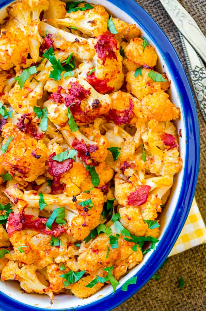 Cauliflower roasted with tomato sauce in a white baking pan.