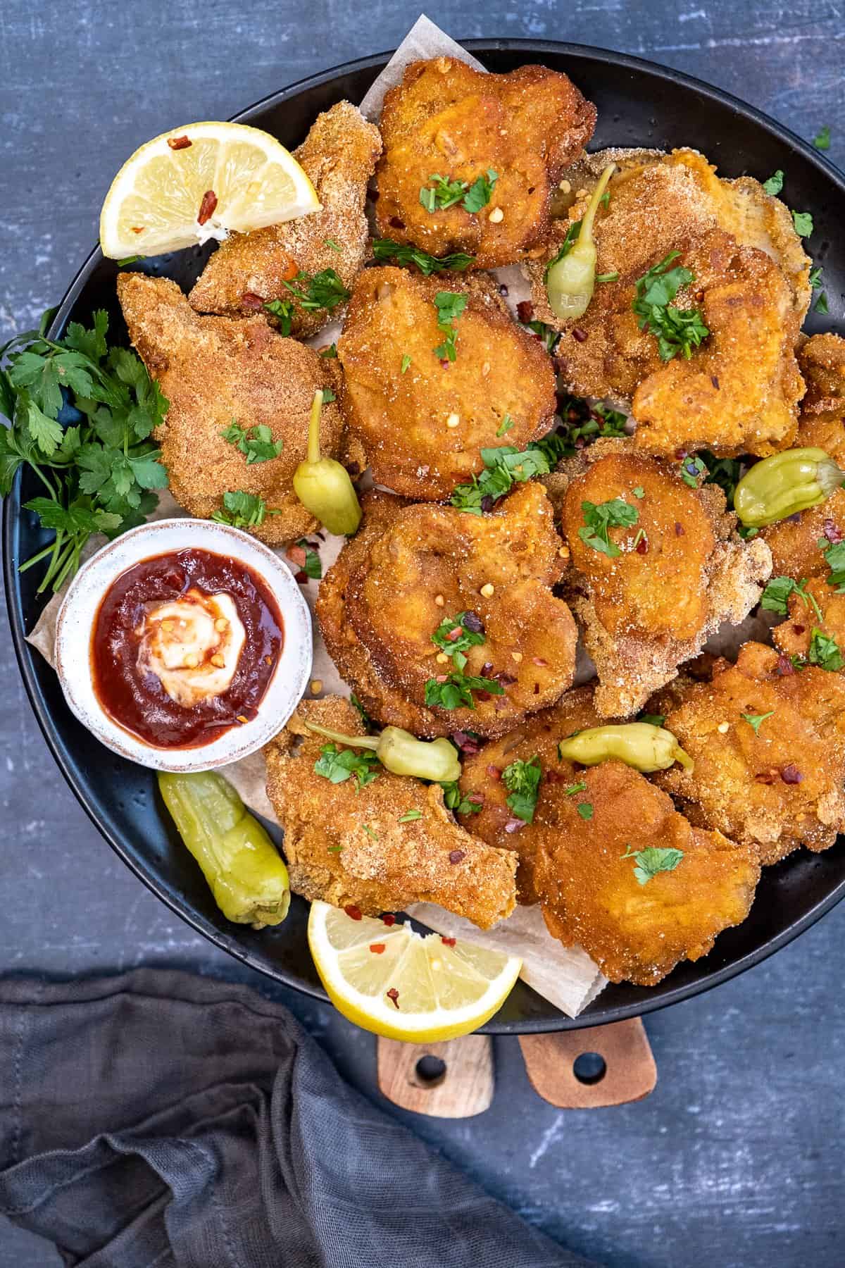 Fried oyster mushrooms served with ketchup and mayo sauce, pickled peppers and lemon wedges on a plate.