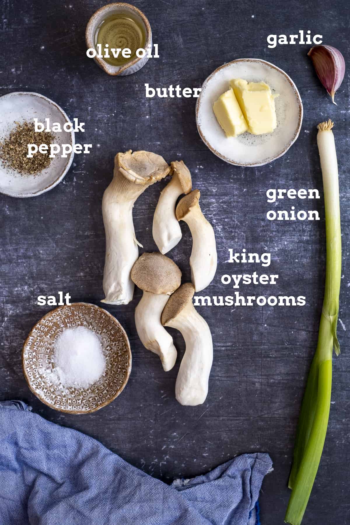 King oyster mushrooms, butter, oil, garlic, green onion, salt and pepper on a dark background.