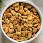 Dried fava beans photographed uncooked in a white bowl.