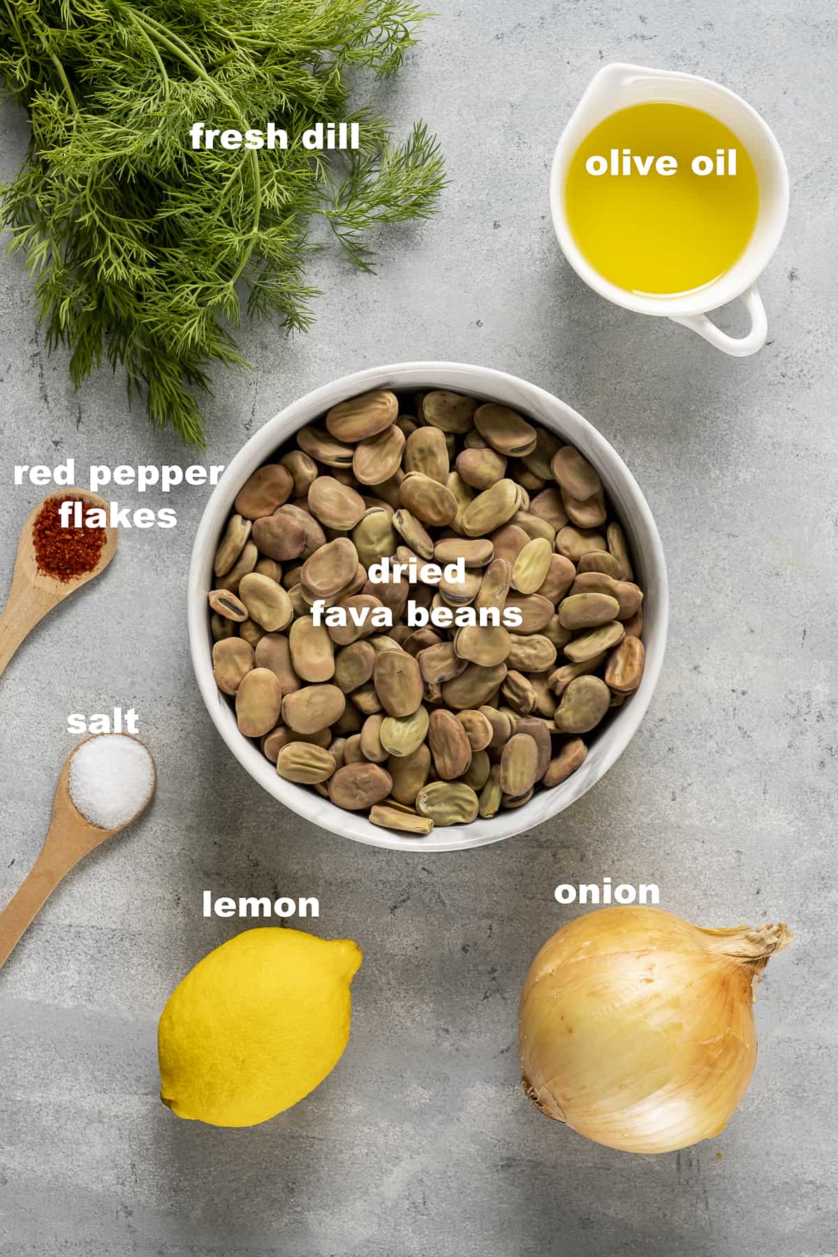 Dried fava beans, olive oil, onion, lemon, fresh dill, salt and red pepper flakes on a grey background.