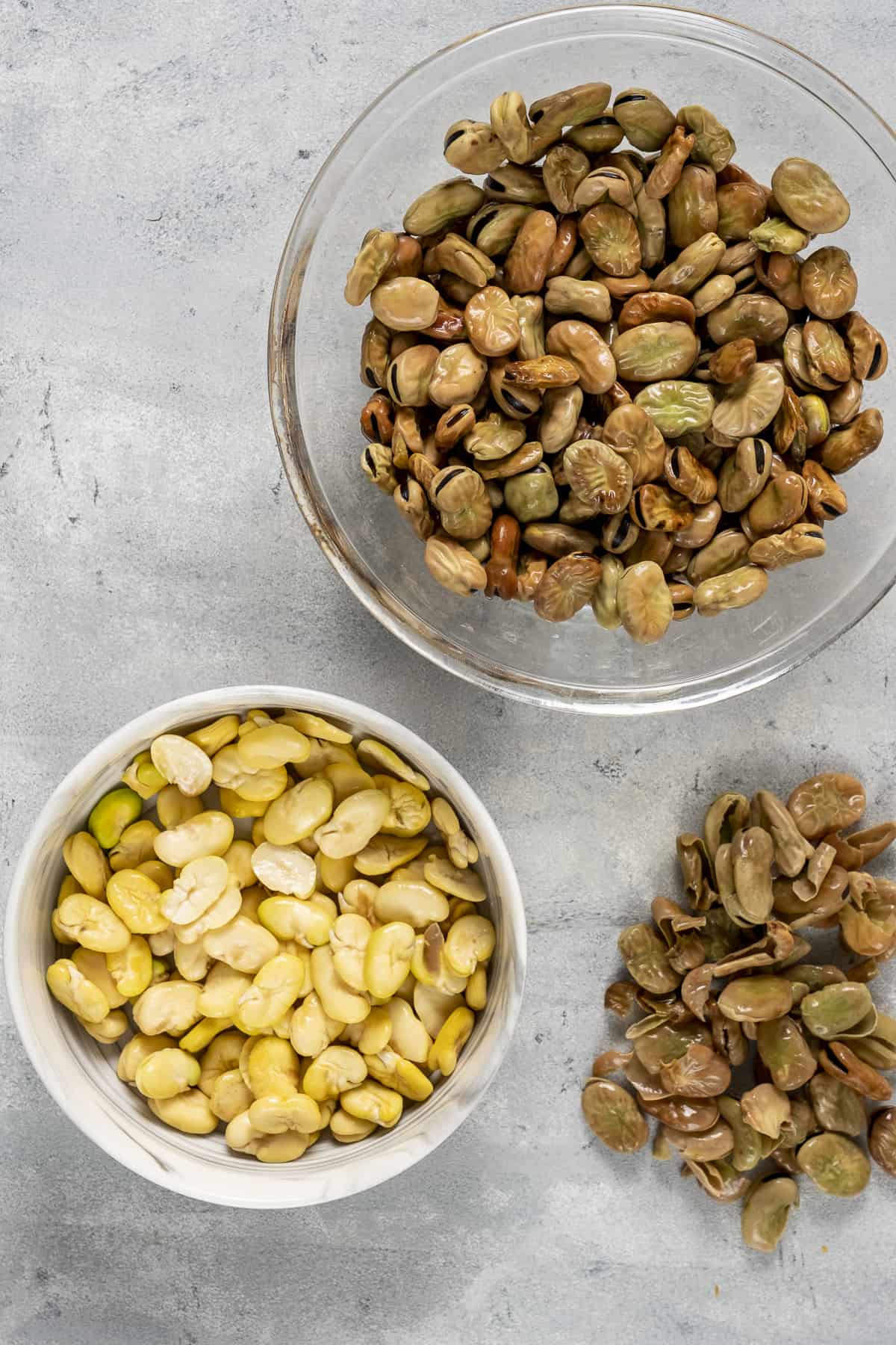 Dried fava beans in two bowls; peeled in one and with skin in the other bowl.