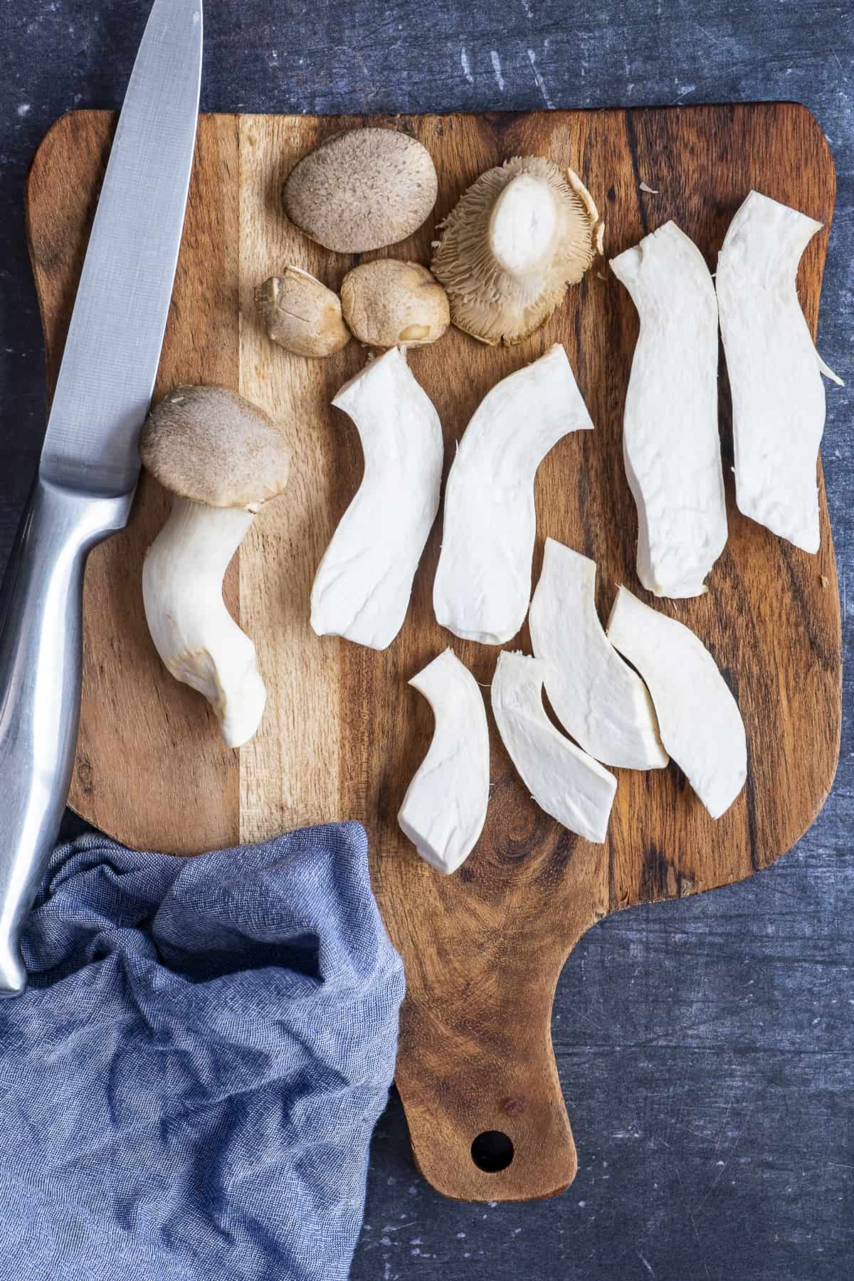 King oyster mushrooms sliced on a wooden board and a knife on it.