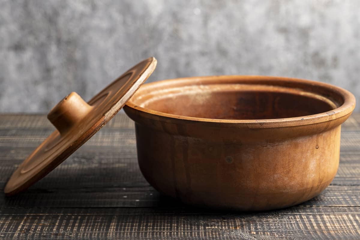 A clay pot and a lid next to it on a wooden table.