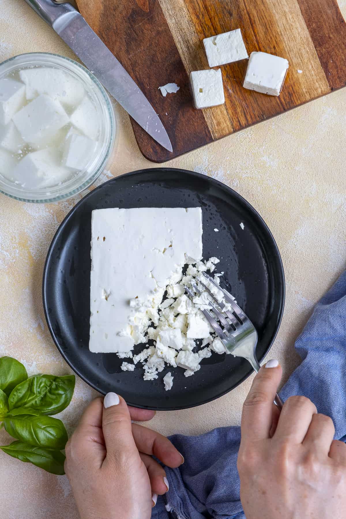 Hands breaking feta cheese with fork.