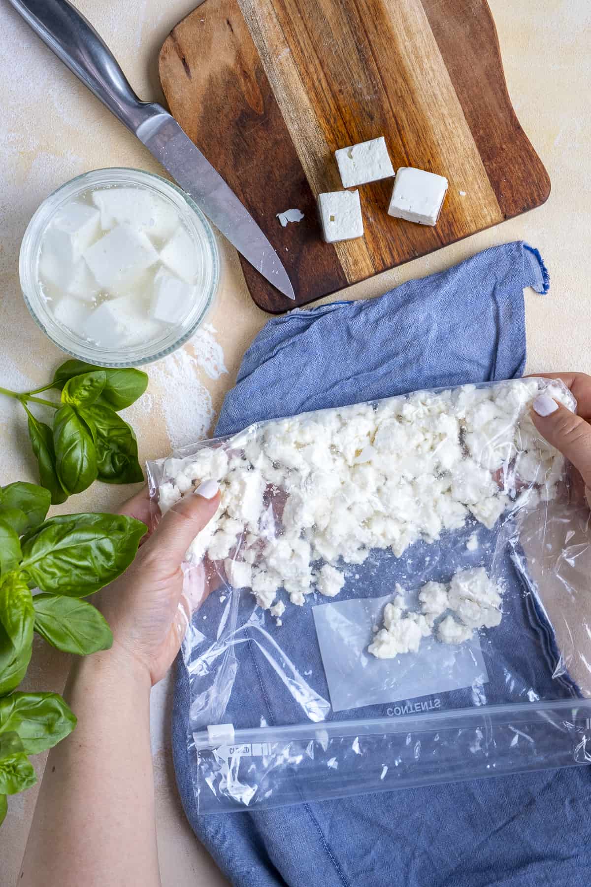 Hands showing how to crumble feta cheese in a freezer bag.