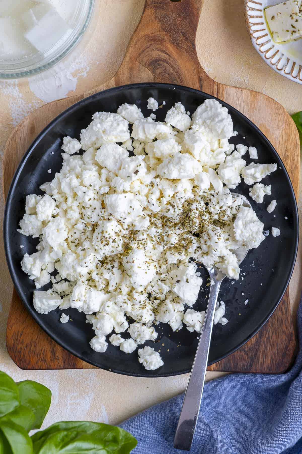 Crumbled feta cheese seasoned with oregano on a black plate with a spoon in it.