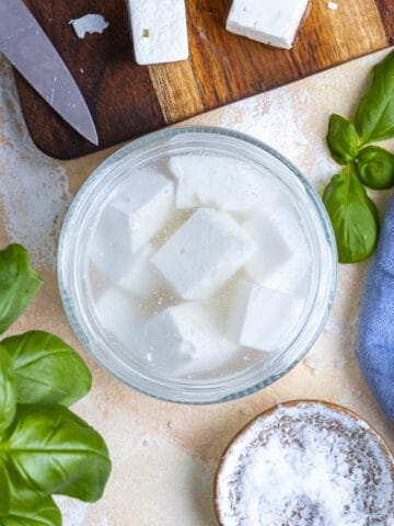 Feta cheese stored in brine in a jar, kosher salt on the side.