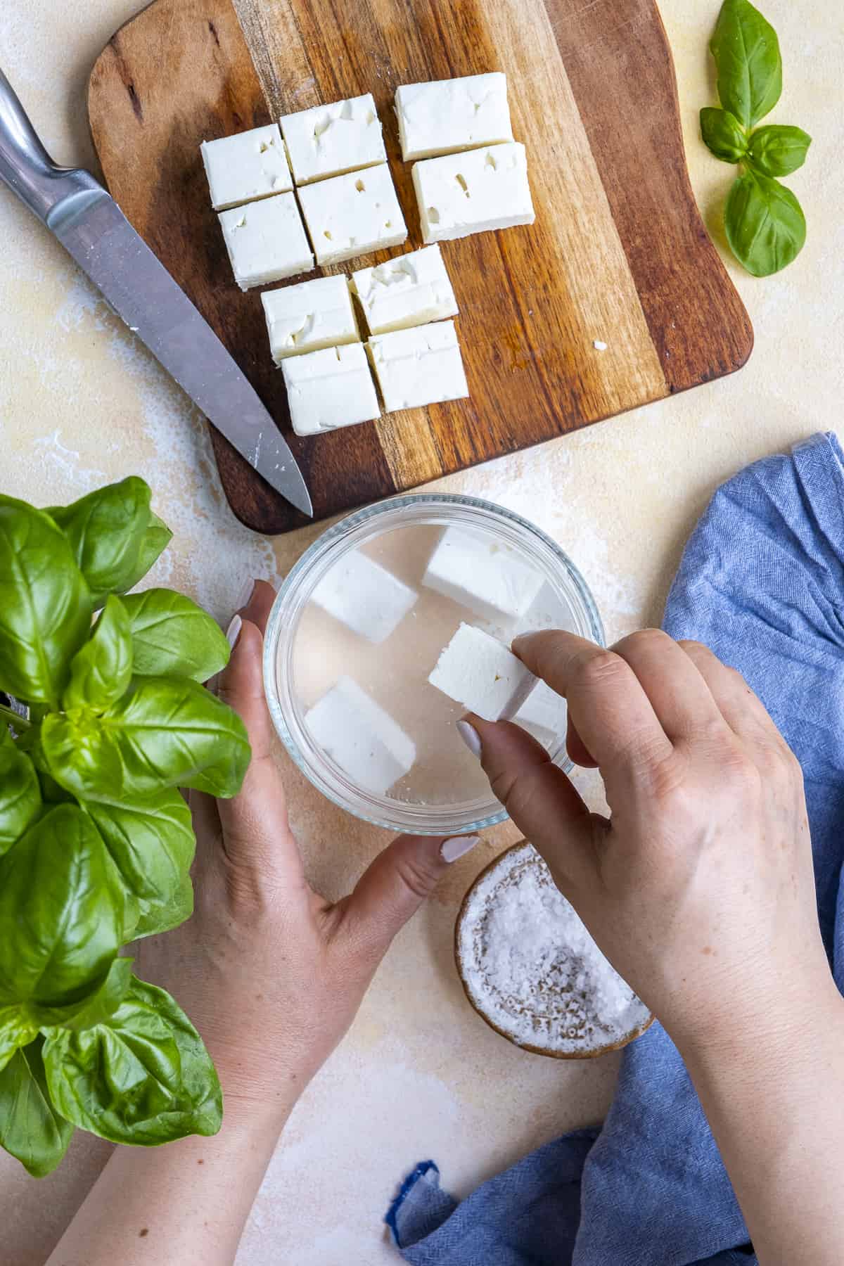 Hands putting feta cheese in brine.