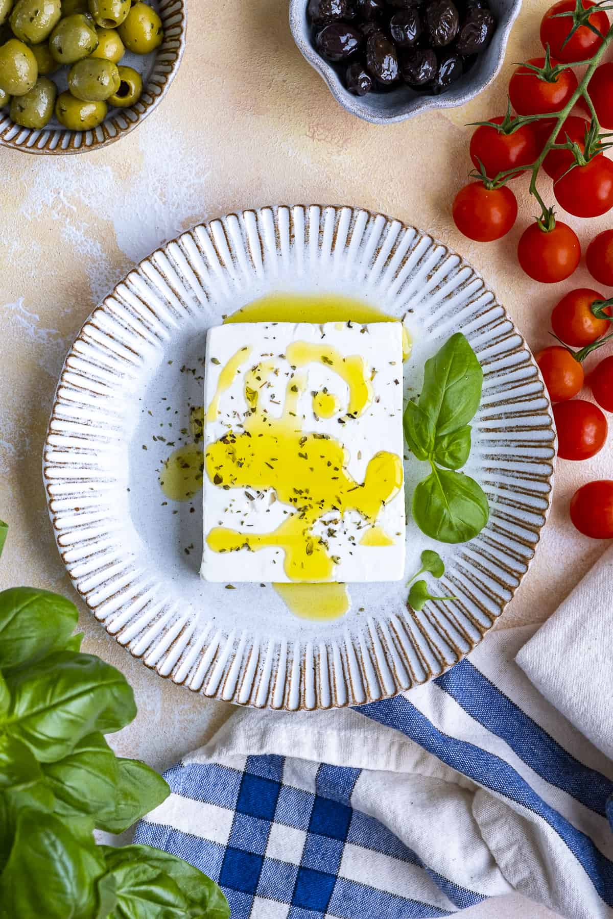 A block of feta cheese garnished with oregano, olive oil and fresh basil on a white plate.