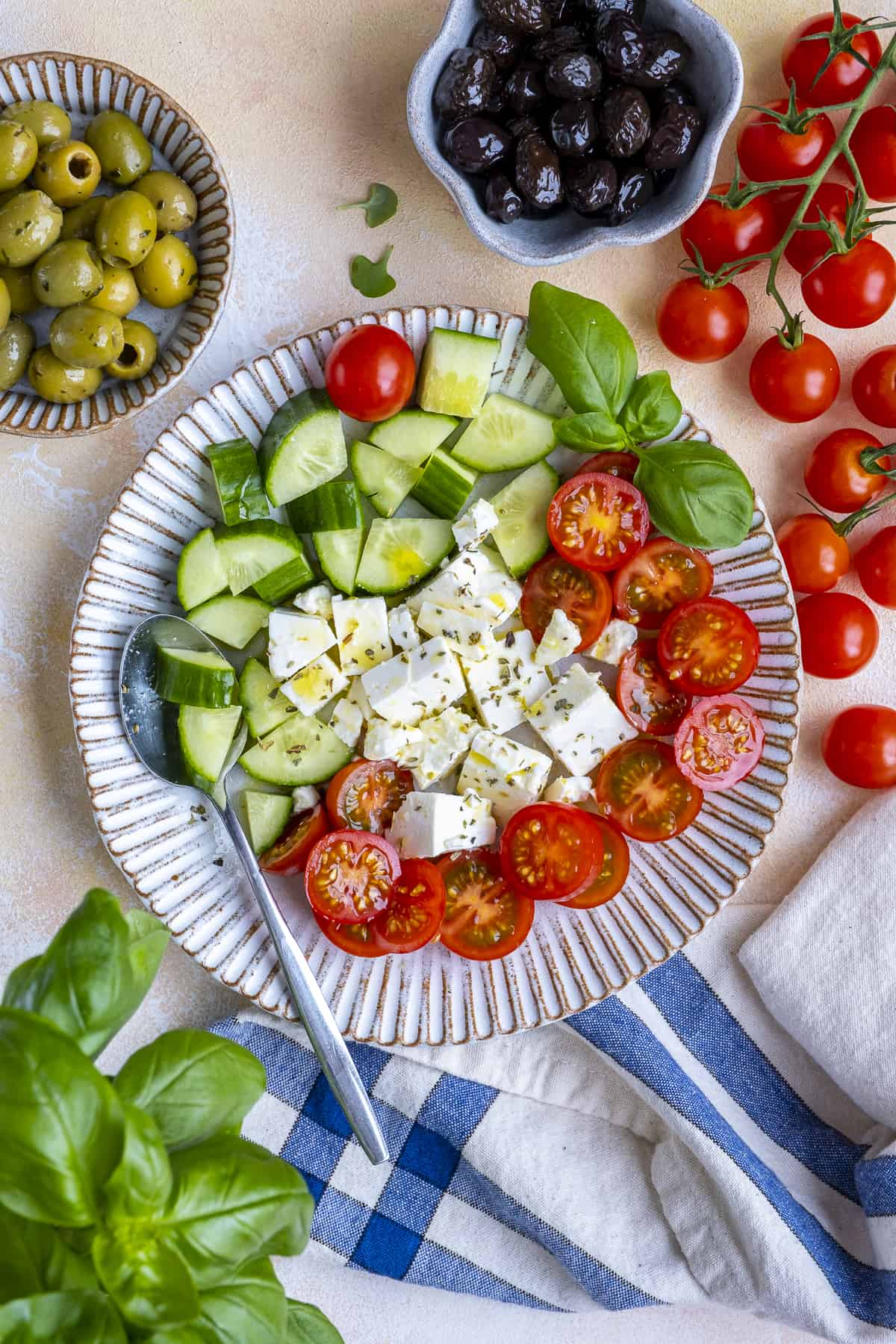 A simple salad with feta cheese, cucumber, tomatoes and fresh basil on a white plate.