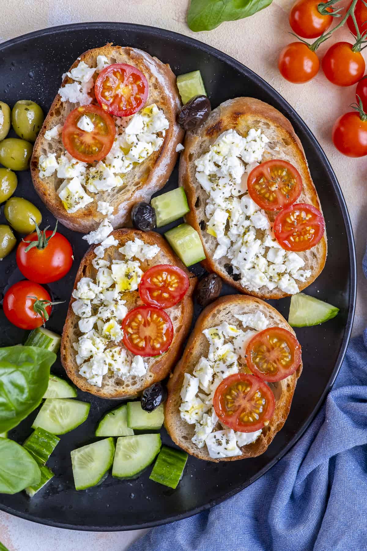 Small open sandwiches topped with feta crumbles and tomatoes on a black plate.