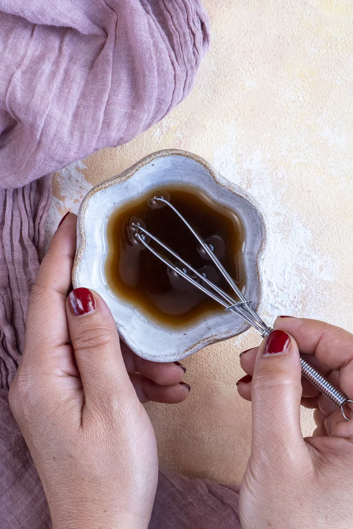 Hands whisking salad dressing in a small bowl.