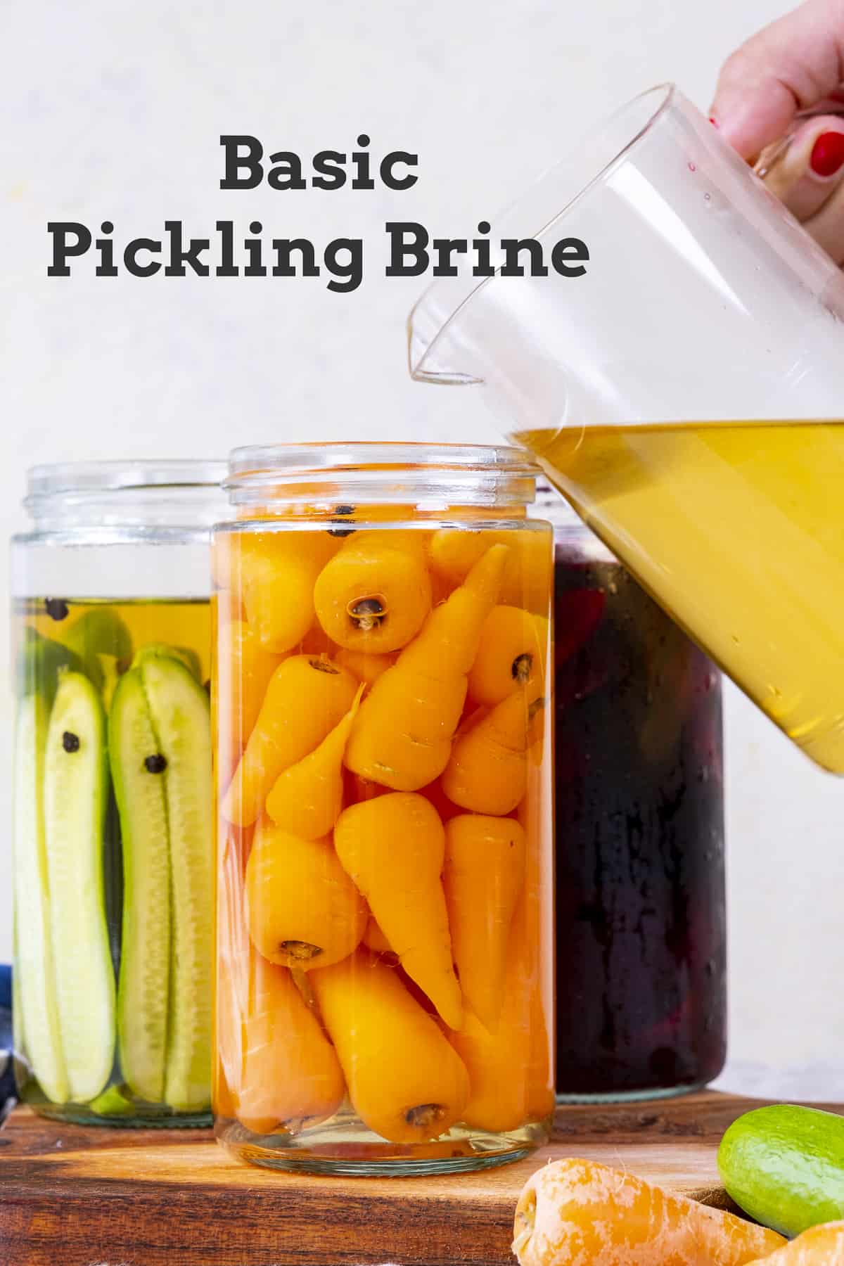 Hand pouring pickle brine over vegetables in jars.