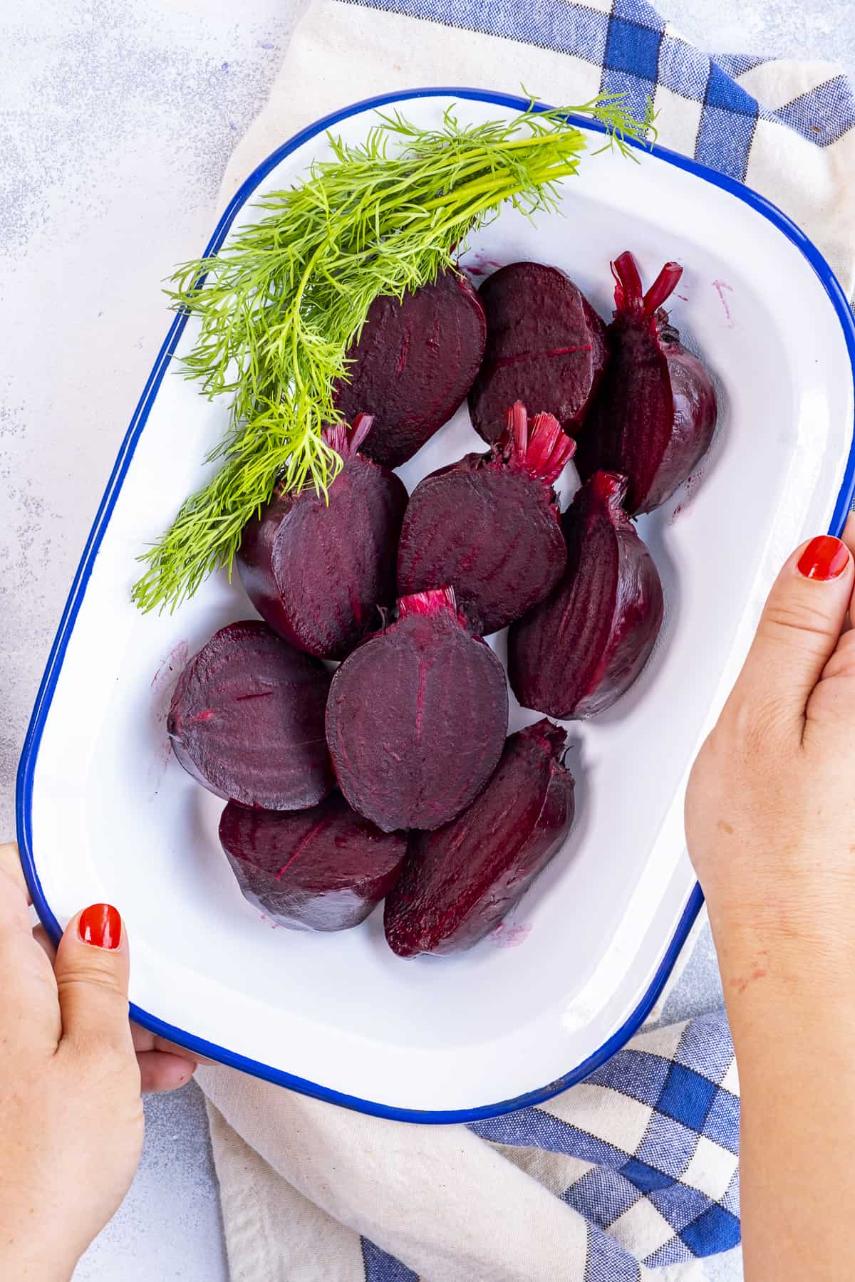 Hands serving halved boiled beets in a white serving dish.