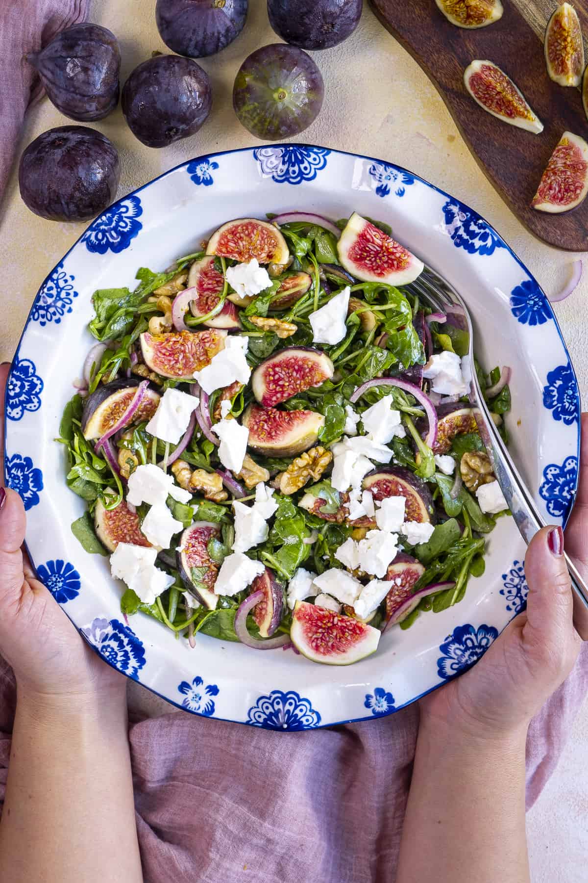 Hands holding a bowl of fig salad with arugula and goat cheese.