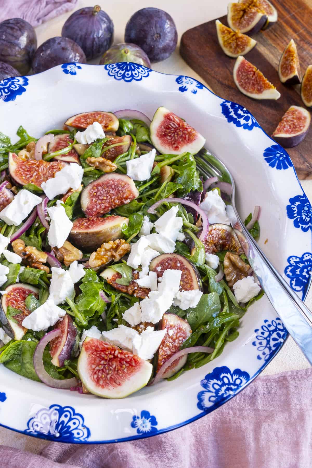 Fig and arugula salad in a white bowl, fresh figs around it.