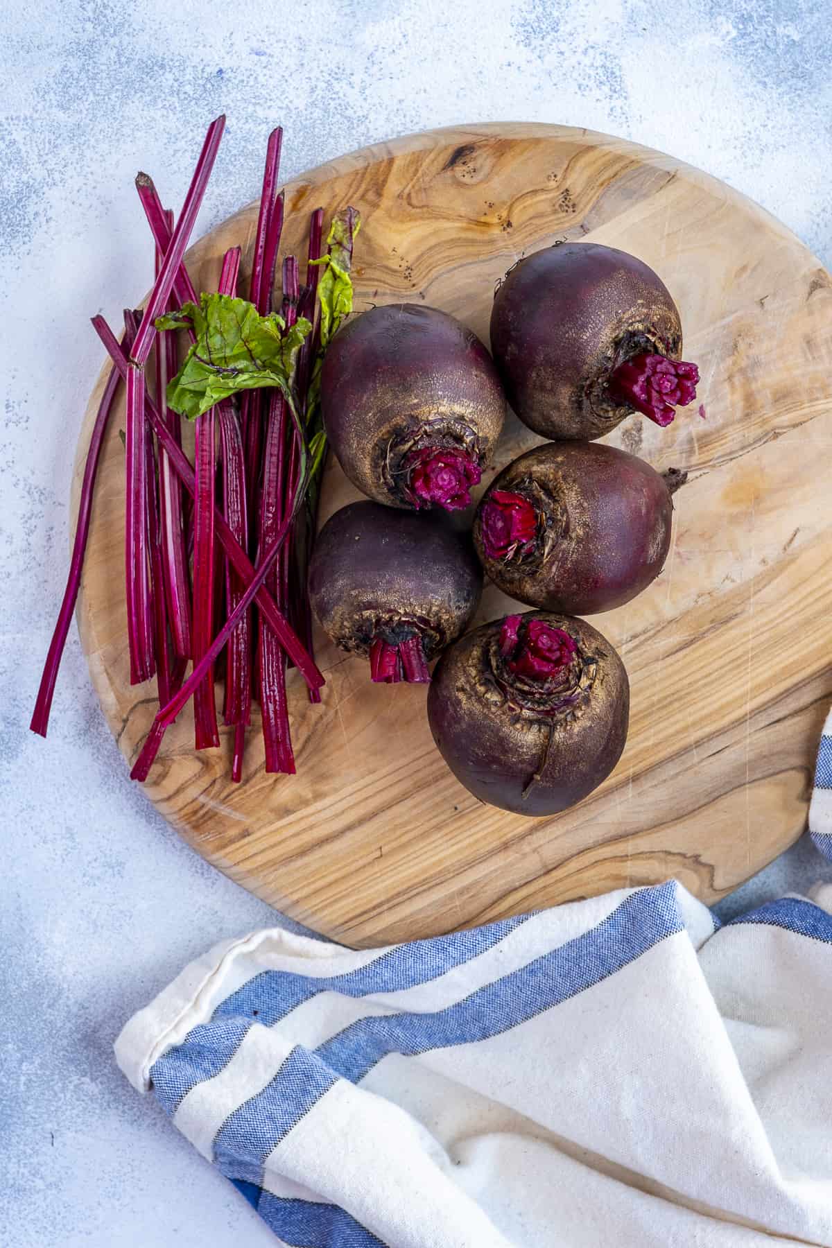 Raw beets on a wooden cutting board and their stems removed on the side.