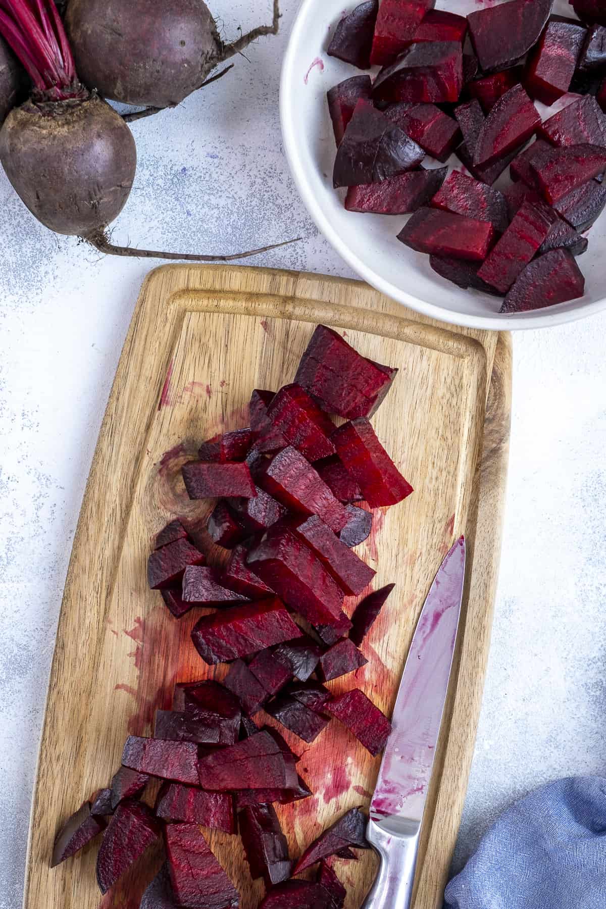 Roasted beets peeled and chopped on a wooden board.