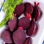 Plate of boiled beets cut in halves, showing their deep red color, garnished with fresh dill.