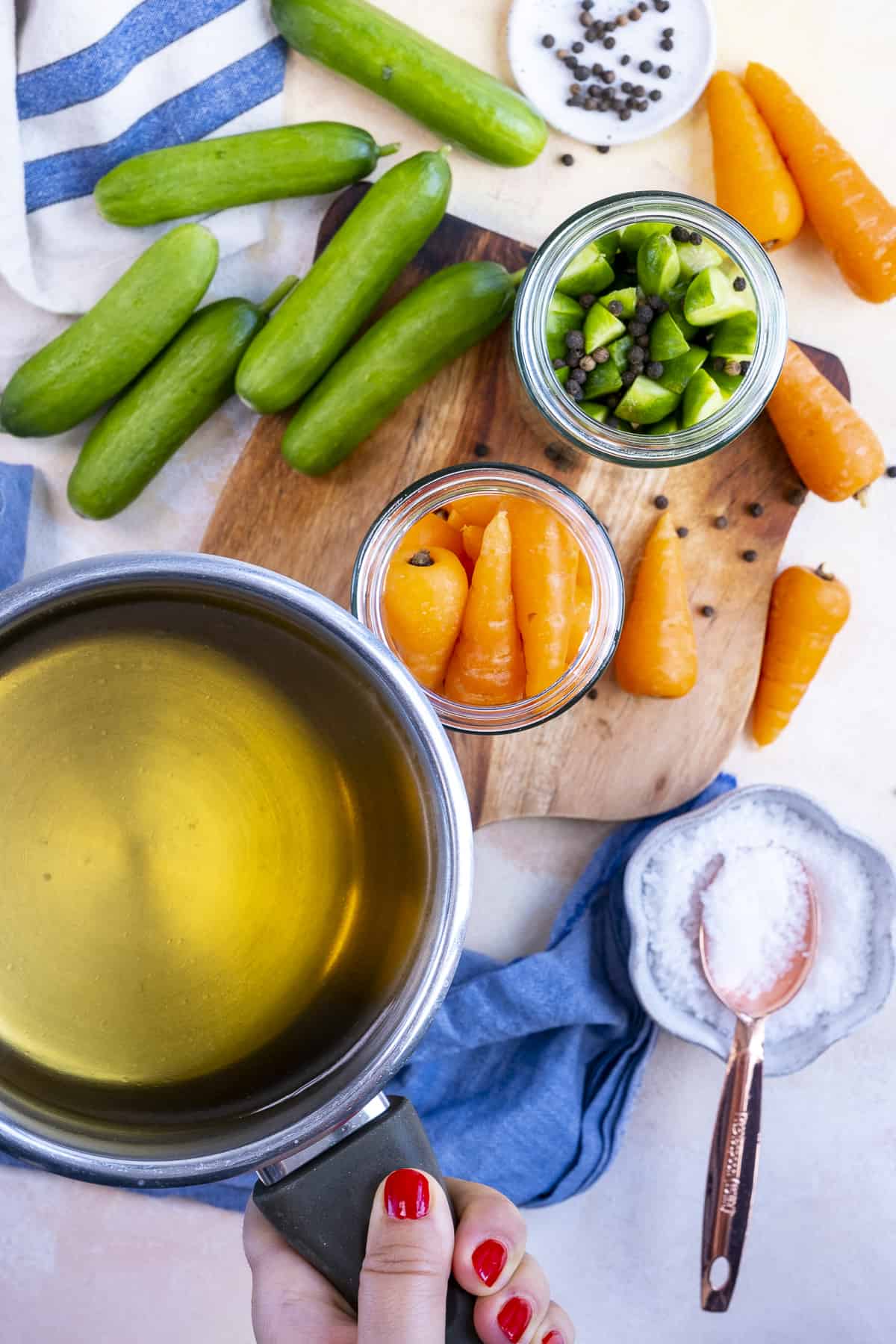 Hand pouring pickle brine into jars with carrots and cucumbers.