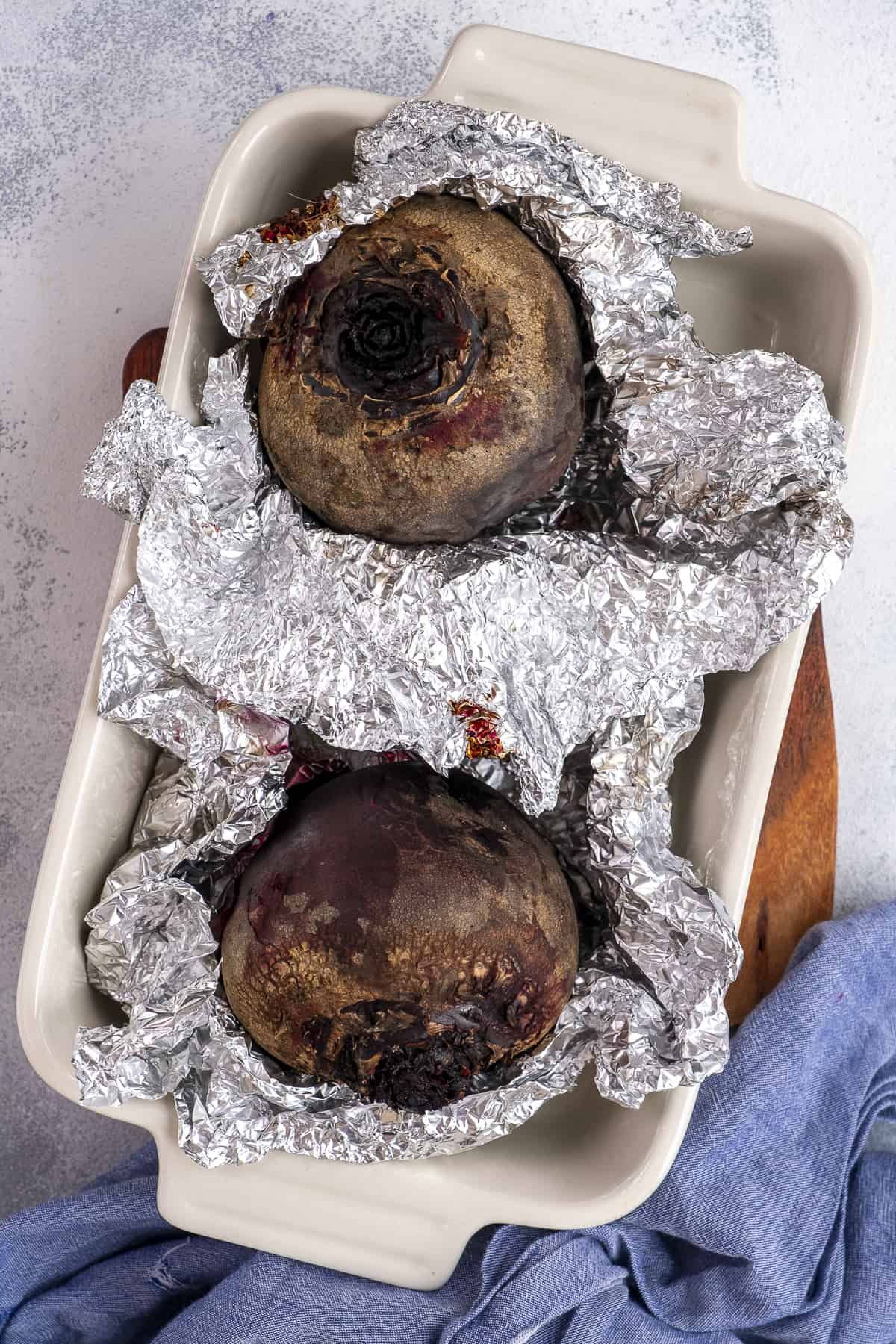 Two beets in separate foil packs in a baking pan.