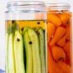 Jars filled with cucumbers and carrots in pickling brine for homemade pickles.