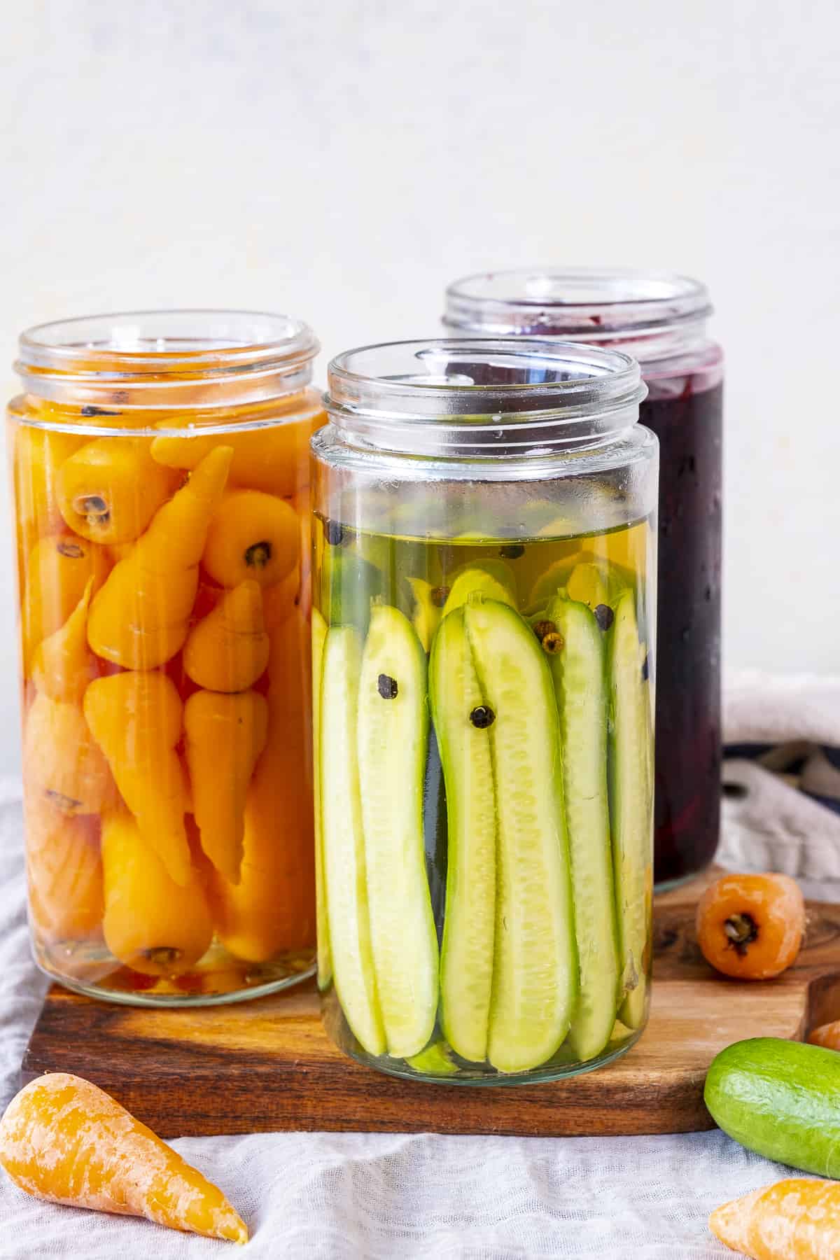 Pickled cucumbers, carrots and beets in jars on a wooden board.