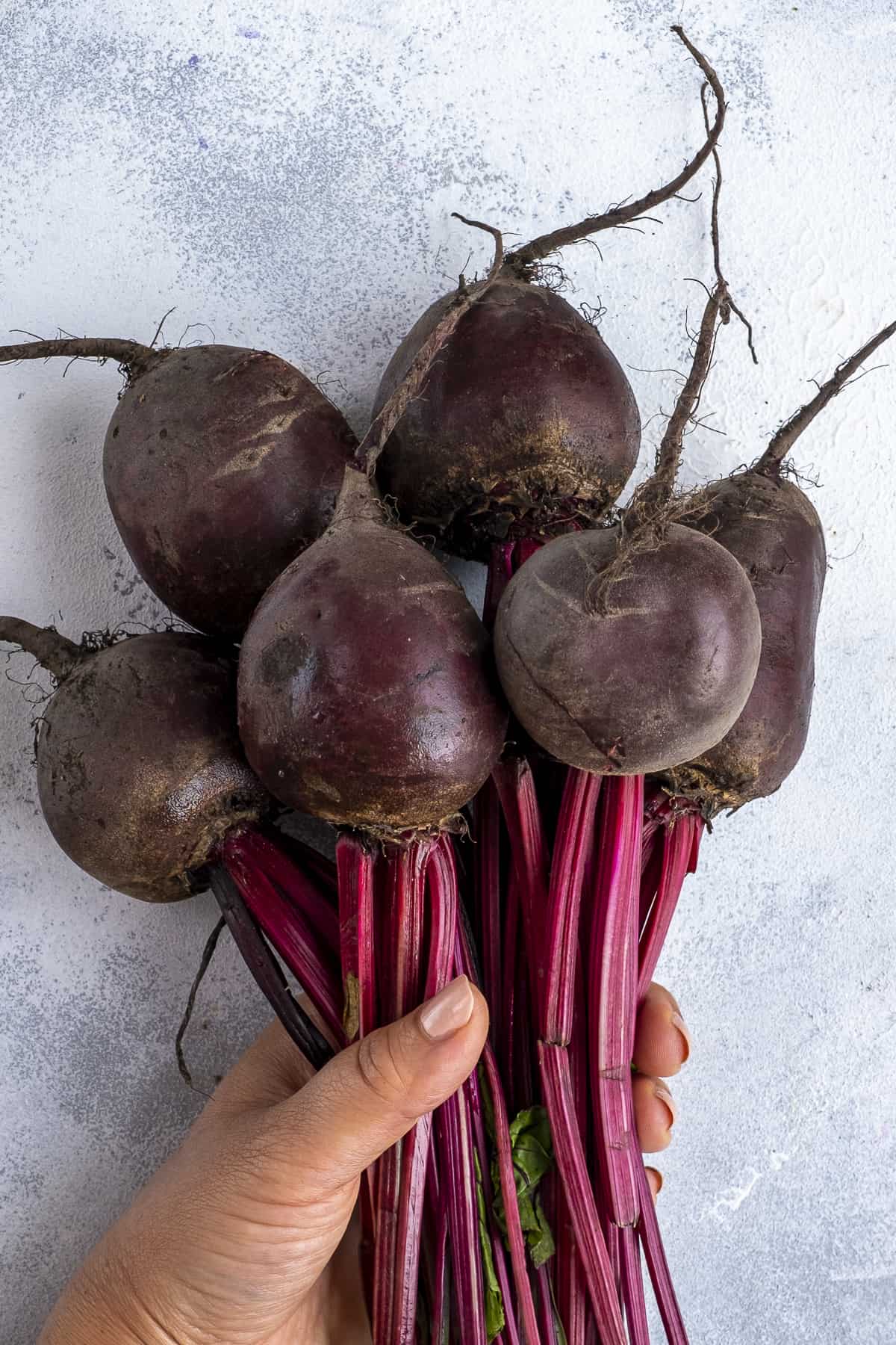 A hand holding raw beets from their stems.