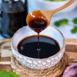 Reduced balsamic vinegar in a white bowl and a wooden spoon pouring some of it.
