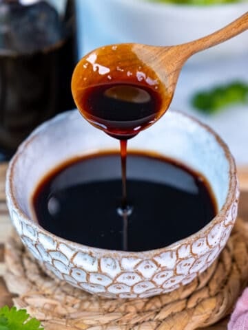 Reduced balsamic vinegar in a white bowl and a wooden spoon pouring some of it.