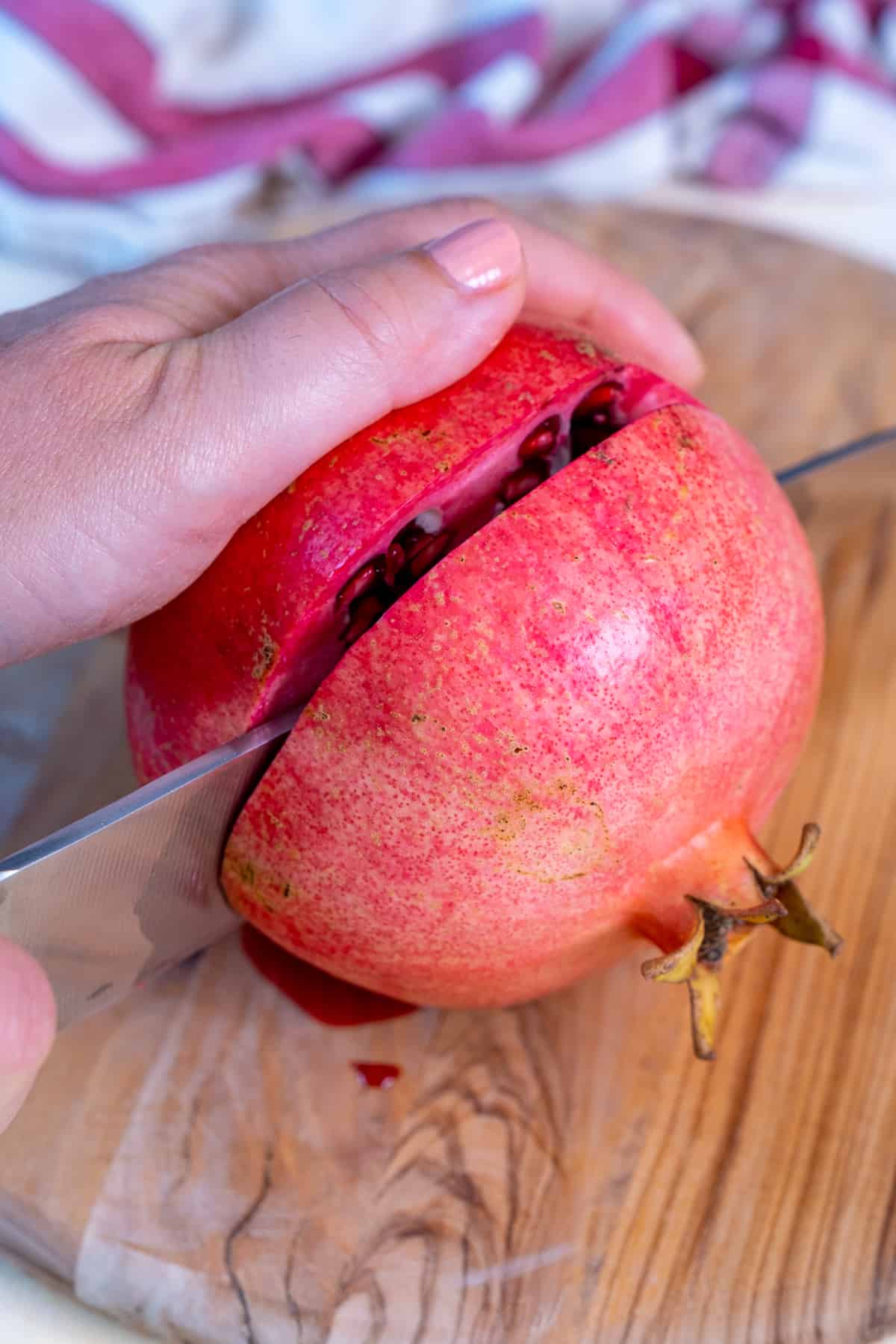 Hands showing how to cut a pomegranate into two horizontally.