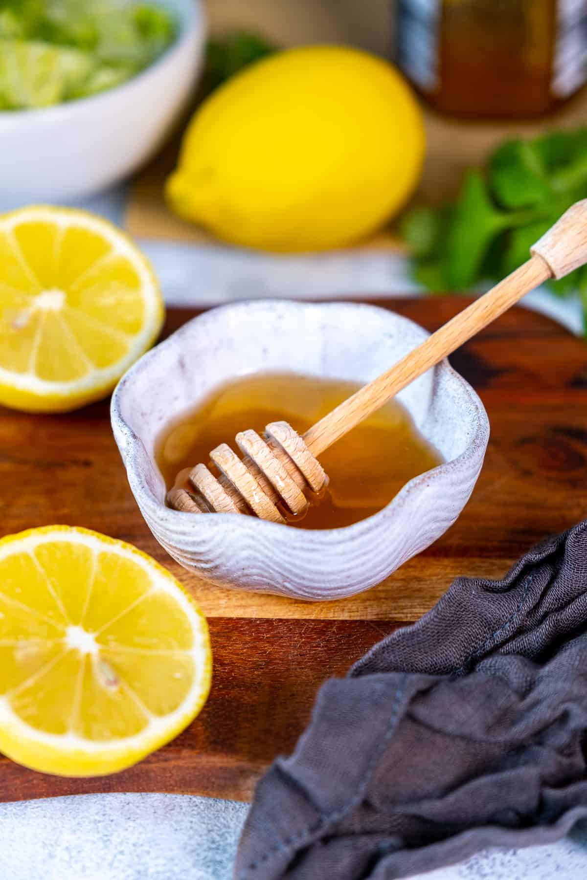 Hone in a small white bowl, a honey dipper inside it and lemons around it.