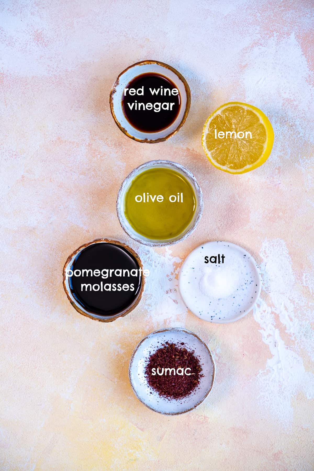 Vinegar, pomegranate molasses, lemon, salt, sumac, olive oil on a light background.