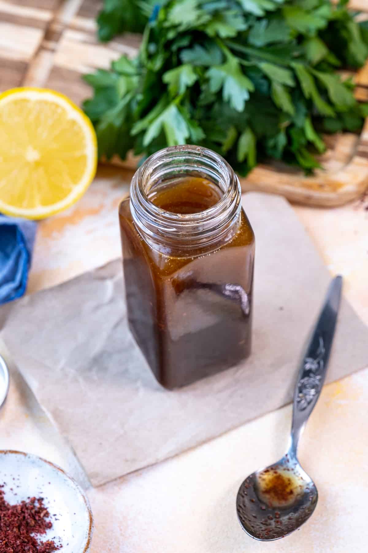 A small jar of salad dressing, a spoon, half lemon and parsley on the side.