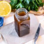 Salad dressing in a small jar, half lemon and parsley behind it.