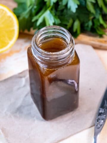 Salad dressing in a small jar, half lemon and parsley behind it.