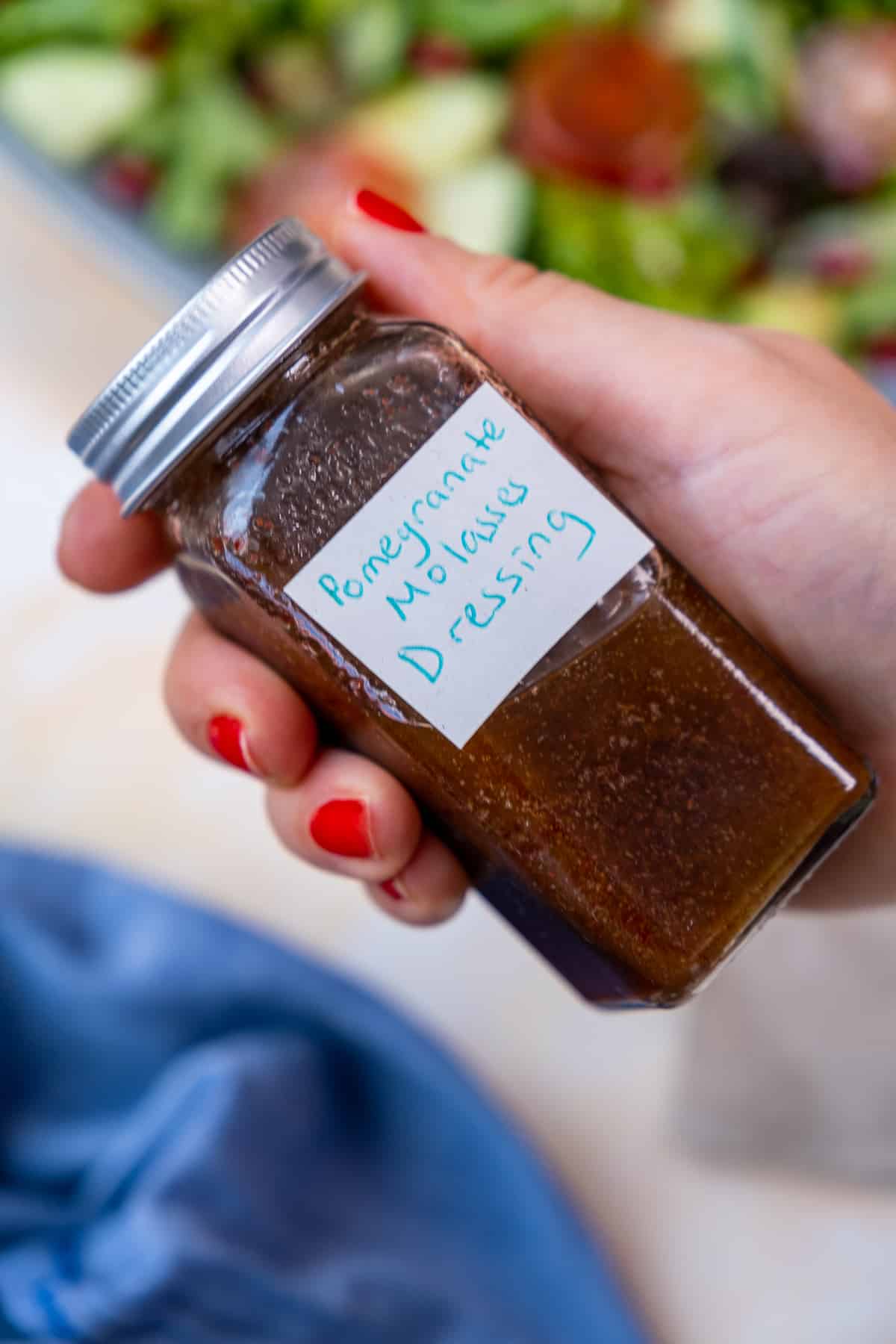 A hand holding a small jar of pomegranate molasses salad dressing.