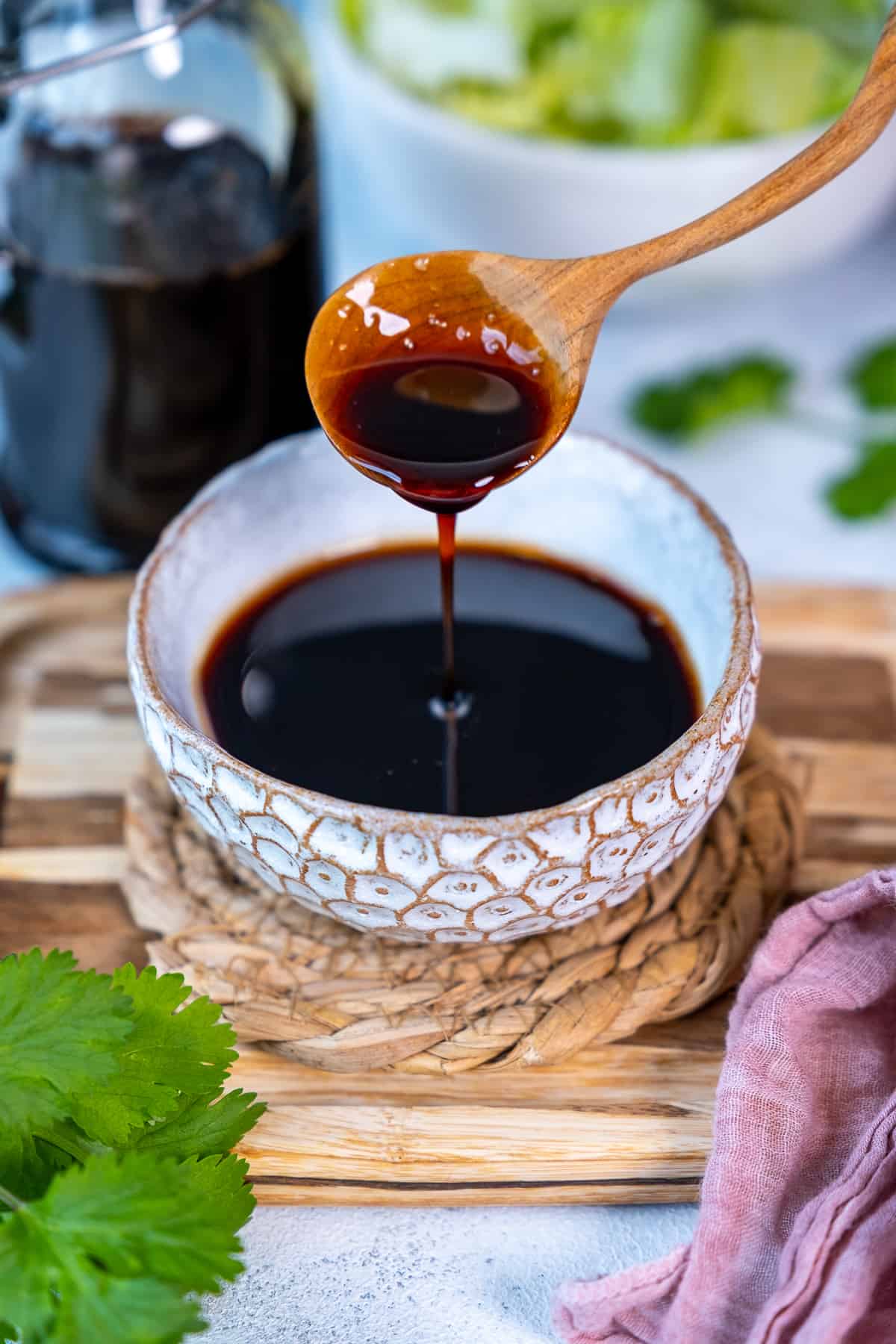 Balsamic vinegar in a white bowl and a wooden spoon pouring some of it.