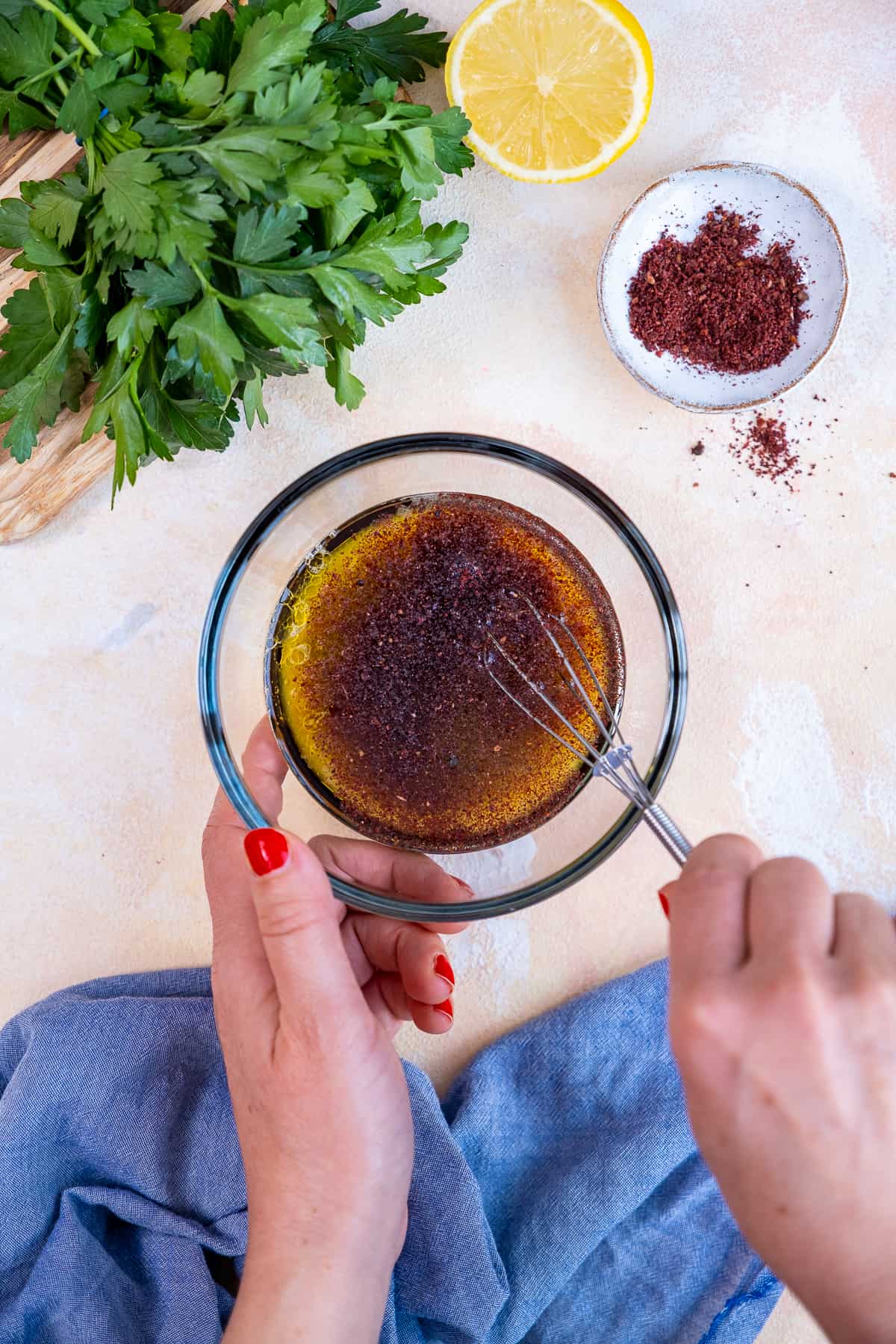 Hands whisking ingredients in a glass bowl to make pomegranate salad dressing.