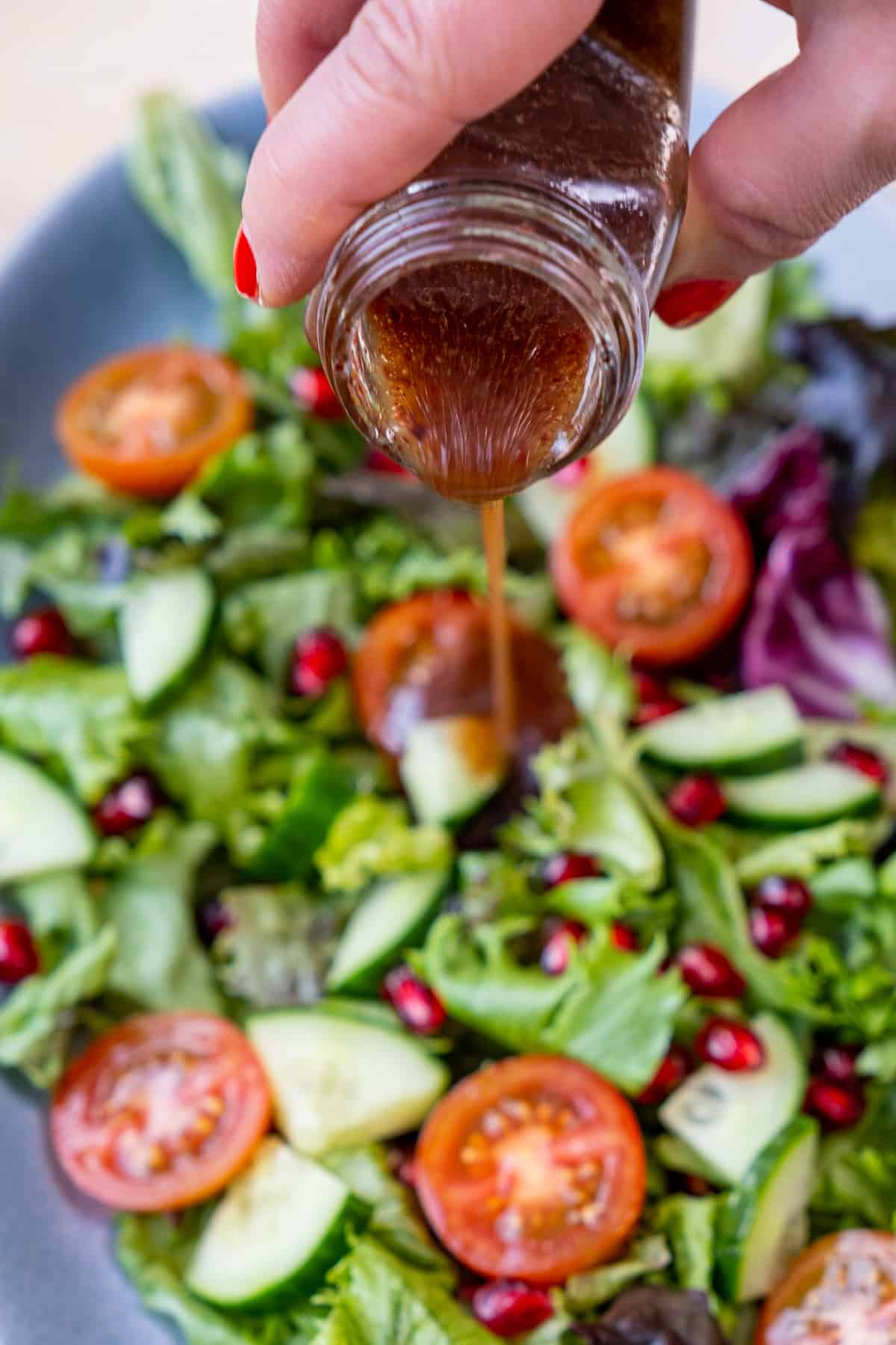 A hand pouring salad dressing from a jar on a green salad.