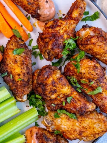 Chicken wings served with carrot and celery sticks and a dipping sauce on a plate.