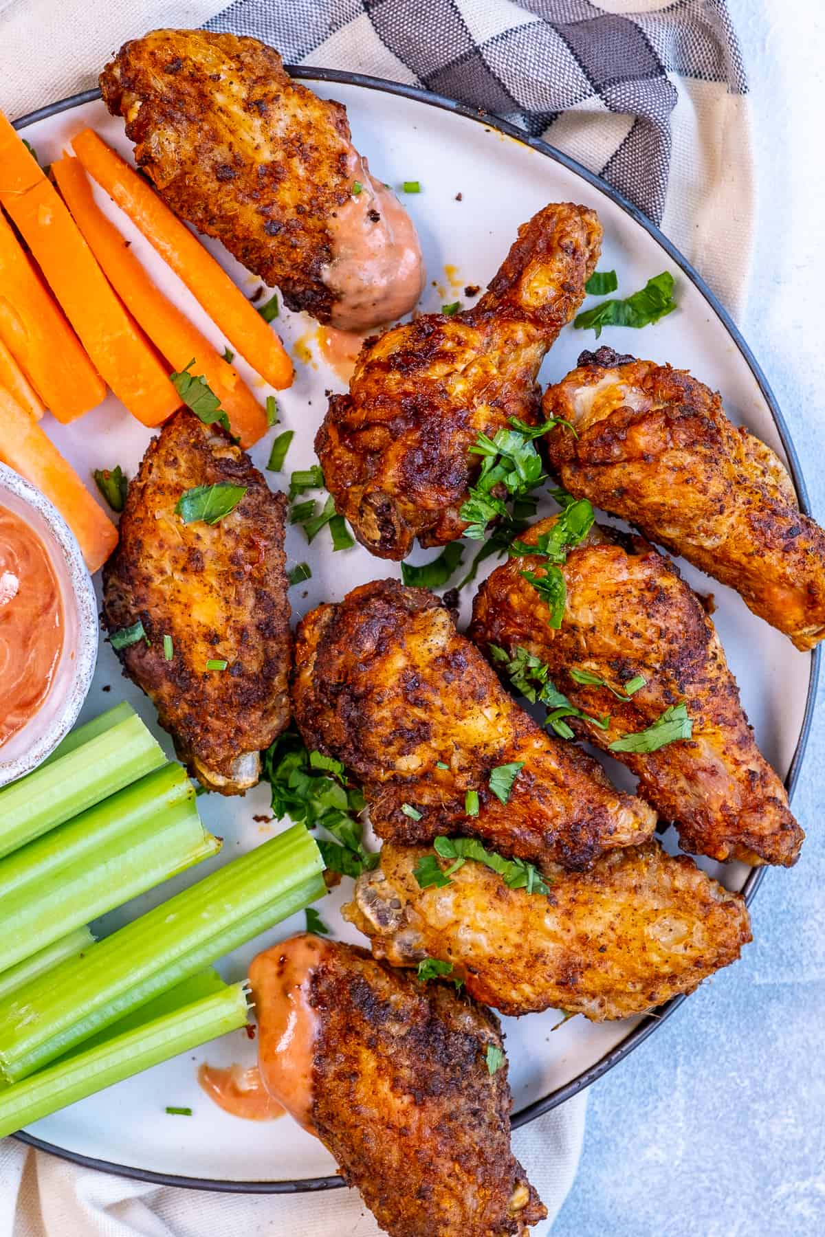 Chicken wings, celery sticks, carrot sticks and a red dipping sauce on a white plate.