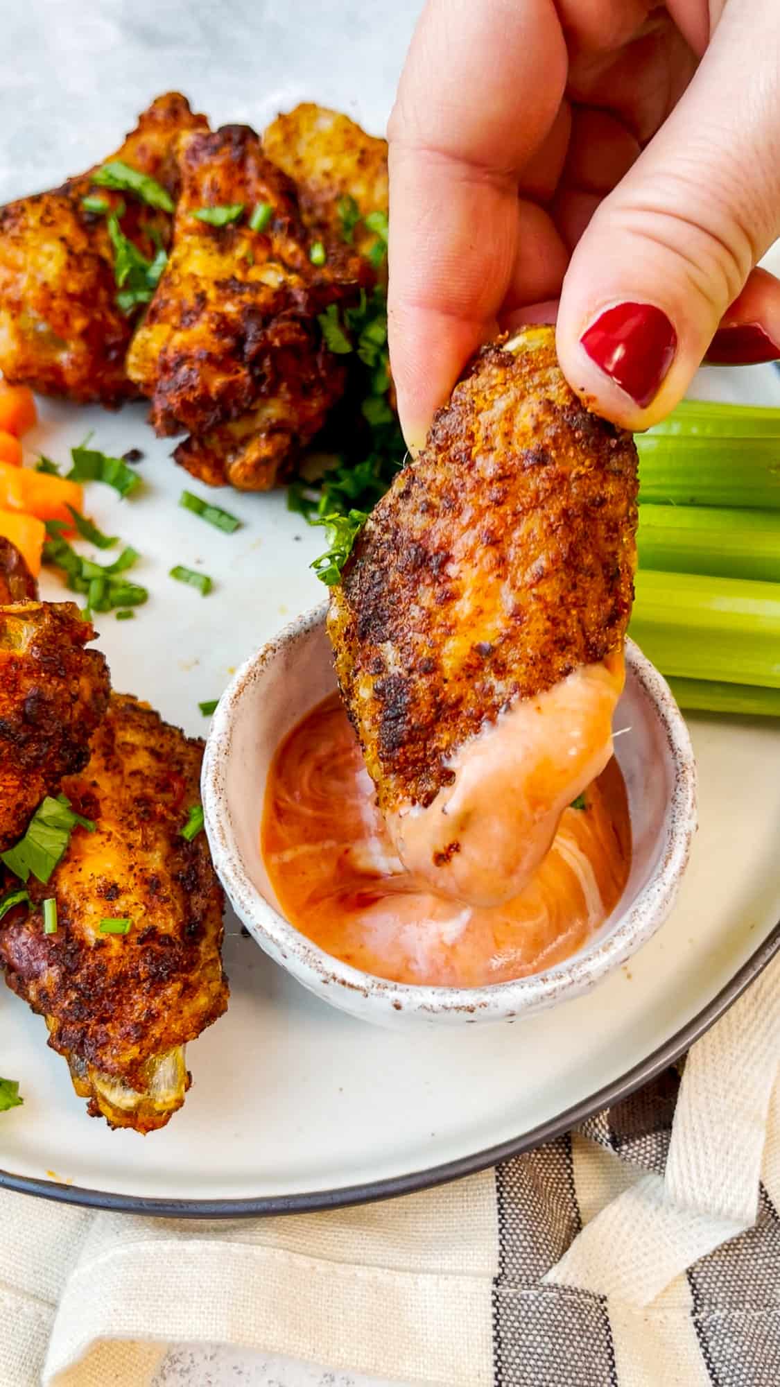 A hand dipping a chicken wing in a dipping sauce.