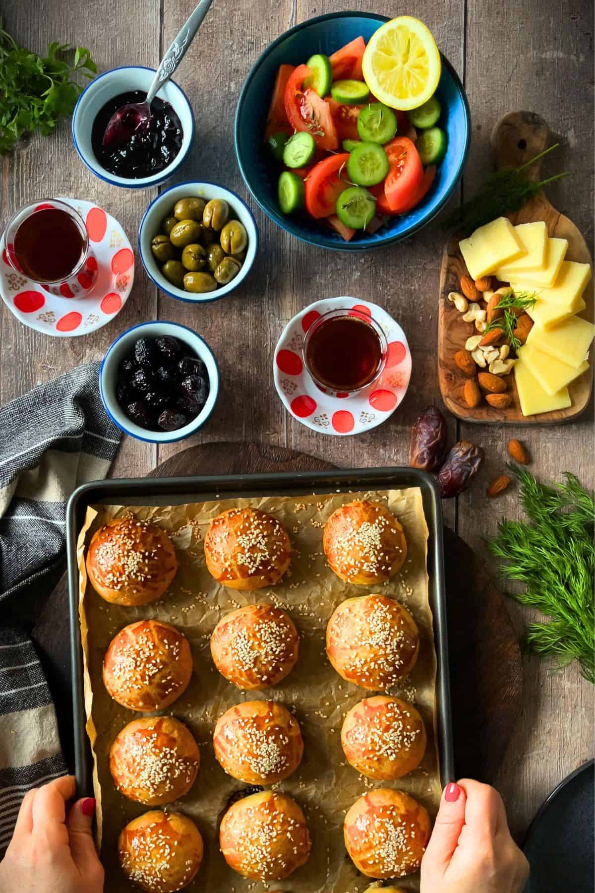 Turkish breakfast table with freshly baked pogaca, olives, cheese, tomatoes, cucumbers, jam, nuts, and Turkish tea.