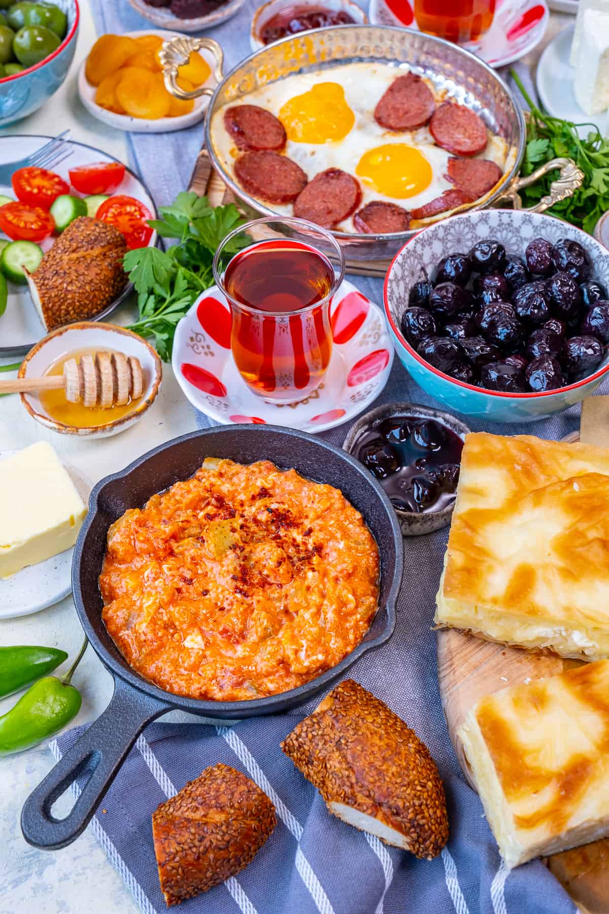 Turkish breakfast with menemen, eggs and sujuk, olives, jams, simit, borek, butter, honey, salad and Turkish tea.