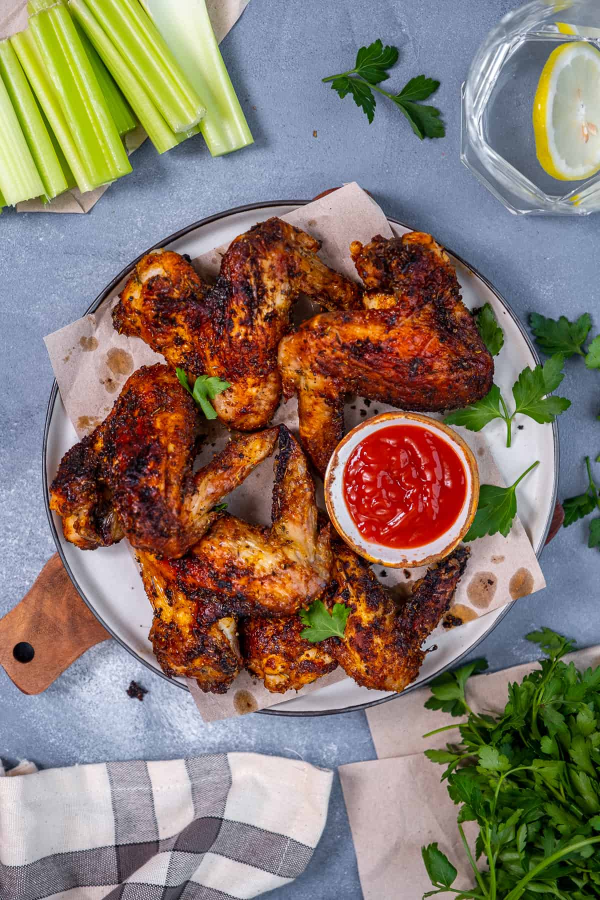 Whole chicken wings garnished with parsley and served with hot sauce on a white plate, celery sticks on the side.