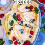 Crepes served with a little powdered sugar, fresh berries and mint leaves on an oval plate.